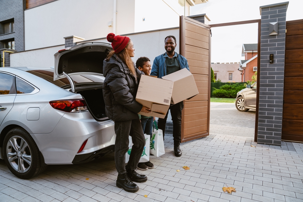 Family unloading car with boxes and walking towards new house
